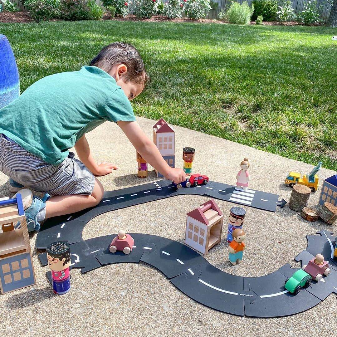 Child playing outdoors with wooden figures on a toy road